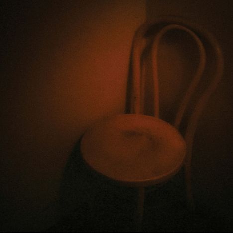 Ein unscharfes Foto zeigt einen einsamen Stuhl im dunklen Raum, schwach beleuchtet in warmem, rötlichem Licht.