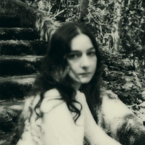 Keine erkennbaren Texte. Verschwommene schwarz-weiße Fotografie einer Frau vor moosbewachsenen Treppen.