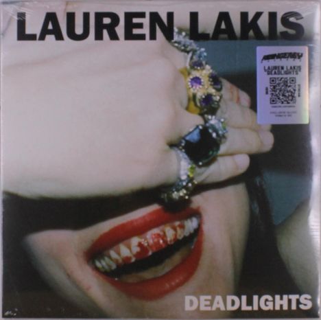 Text: "LAUREN LAKIS" oben, "DEADLIGHTS" unten. 
Nahaufnahme eines Gesichts mit rot geschminkten Lippen und dekorierten Ringen.