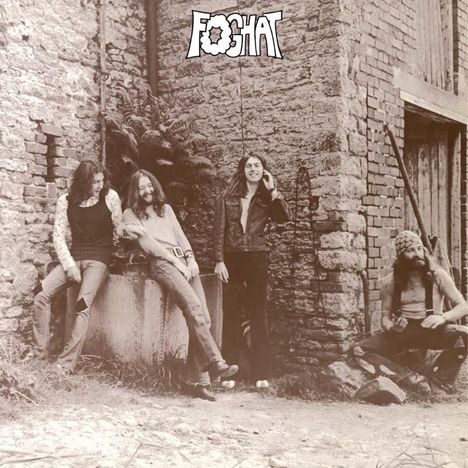 Text: "FOGHAT". Vier Männer lehnen lässig an einer alten Backsteinmauer, zwei stehend, einer sitzend. Retro-Stimmung.