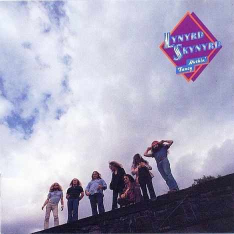 Text: "Lynyrd Skynyrd Nuthin’ Fancy". Sieben Personen stehen auf einer dunklen Fläche vor einem bewölkten Himmel.