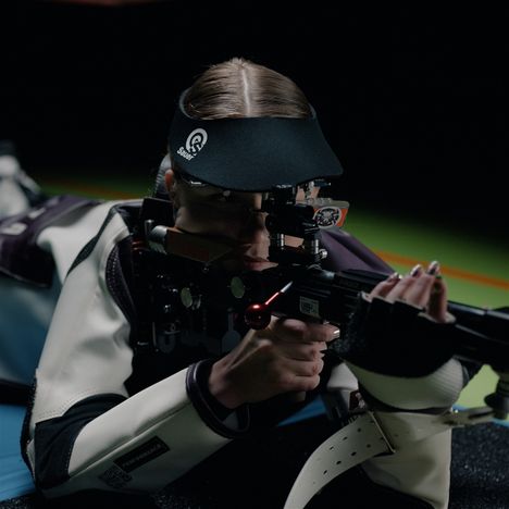 Eine Person zielt mit einem Gewehr. Sie trägt eine Mütze mit Logos von "Sauer" und "Performance".