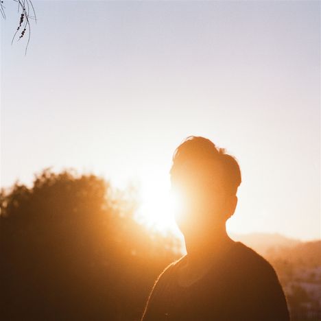 Eine Silhouette einer Person vor einem hellen, tief stehenden Sonnenuntergang, umgeben von Bäumen.