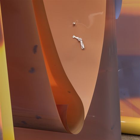 Keine erkennbaren Texte. Abstrakte Skulptur mit geschwungenen, orange-braunen Flächen und einem kleinen, silbernen Detail.