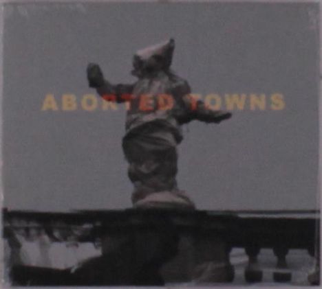 Text: "ABORTED TOWNS". Statue vor trübem Himmel, verhüllte Figur mit ausgebreiteten Armen.