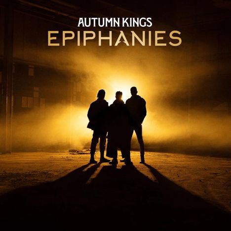 "Autumn Kings EPIPHANIES" steht oben. Drei Silhouetten stehen vor einem intensiven gelben Licht in einem dunklen Raum.