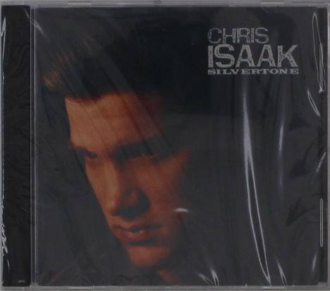 Text: "Chris Isaak Silvertone". Nahaufnahme eines Mannes mit ernstem Blick, in dunklen Farben gehalten.