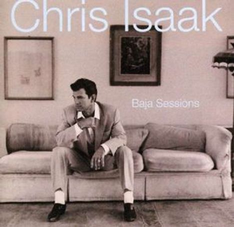 Text: "Chris Isaak," "Baja Sessions." Ein Mann in Anzug sitzt nachdenklich auf einem Sofa, gerahmte Bilder im Hintergrund.