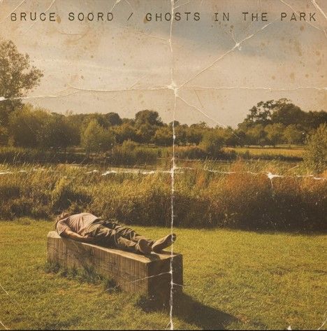 "Bruce Soord / Ghosts in the Park." Eine Person liegt entspannt auf einer Bank, umgeben von grüner Landschaft.