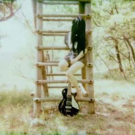 Person sitzt auf Holzleiter in einem sonnigen Wald. Eine schwarze Gitarre lehnt unten an der Leiter.