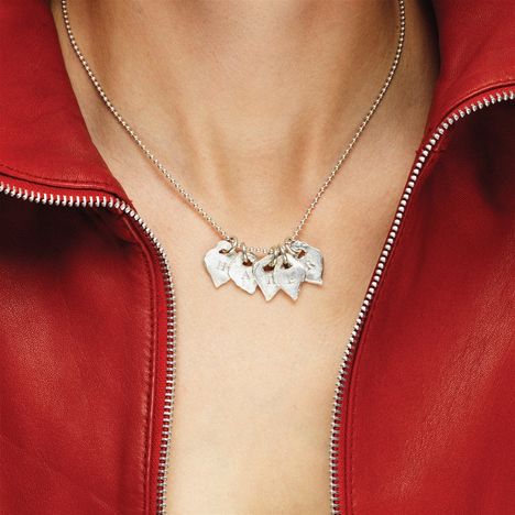 Auf der Halskette sind metallene Anhänger mit den Buchstaben "H A P P Y". Sie liegt über einer roten Lederjacke.