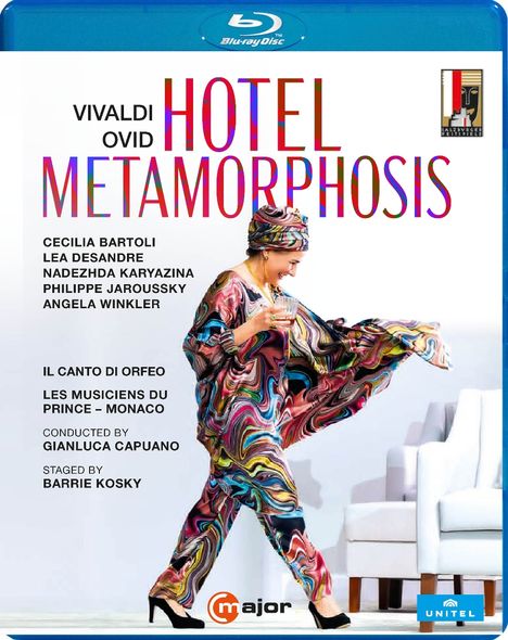 „VIVALDI OVID HOTEL METAMORPHOSIS“, farbige Schrift. Frau in buntem Outfit, hält Glas, posiert neben weißen Sesseln.