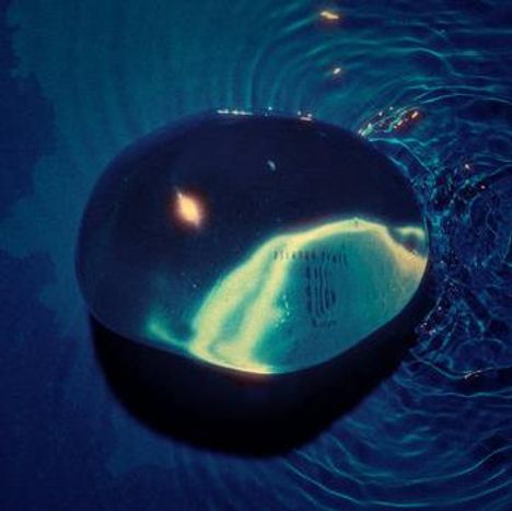 Eine glänzende, transparente Kugel liegt auf einer welligen Wasseroberfläche, umgeben von blauem Licht.