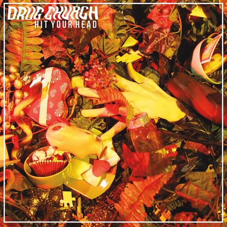 "DRUG CHURCH" und "HIT YOUR HEAD" stehen oben. Ein wirres Arrangement aus Blättern, Spielzeug und farbigen Objekten.