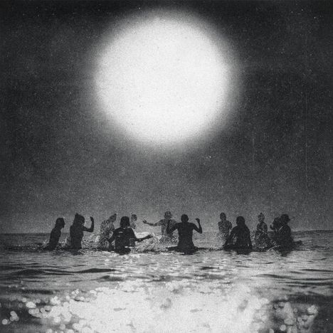 Im Vordergrund spielen mehrere Menschen im Wasser, während ein großer heller Kreis am Himmel leuchtet.