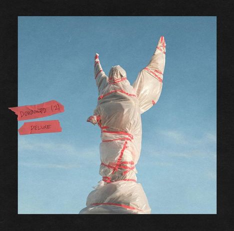 Text: "DOWNWARD (2)" und "DELUXE". 
Eine Statue, in Plastik und rotem Band eingewickelt, mit erhobenen Armen vor blauem Himmel.