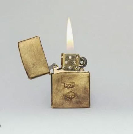 Das goldene Feuerzeug hat den Text "PZF" und ein Emblem. Die Flamme brennt, der Deckel ist offen.
