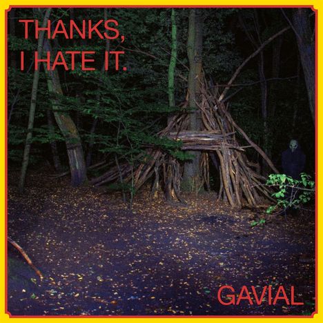 "THANKS, I HATE IT. GAVIAL" in roten Buchstaben. Nachtszene im Wald, Hütte aus Ästen, Person im Dunkeln sichtbar.