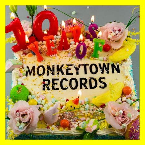 "10 YEARS OF MONKEYTOWN RECORDS" steht auf einer dekorierten Torte mit brennenden Kerzen und bunten Blumen.