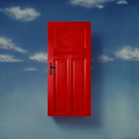 Eine rote Tür schwebt in einem blauen Himmel mit vereinzelten weißen Wolken.