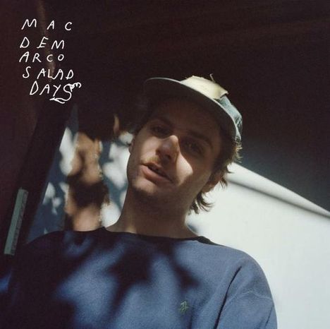 Text: "MAC DEMARCO SALAD DAYS". Ein Mann mit Kappe und Pullover, im Schatten, vor unscharfem Hintergrund.