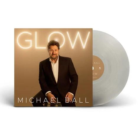 "Glow" und "Michael Ball" auf einem Albumcover. Ein Mann in Anzug sitzt lächelnd. Eine Schallplatte daneben.