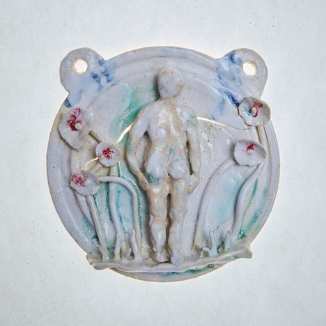 Keramikrelief: zentral eine nackte Figur. Umrahmt von Blumen mit roten Zentren. Hellblaue und grüne Töne dominieren.
