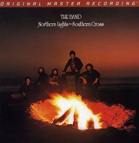 "THE BAND, Northern Lights - Southern Cross." Fünf Männer sitzen um ein Lagerfeuer, der Himmel ist orange gefärbt.