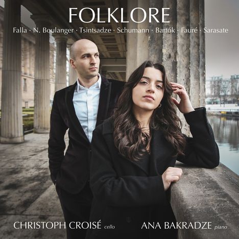"FOLKLORE" oben, Künstlernamen unten. Ein Mann und eine Frau in eleganter Kleidung stehen nebeneinander vor Säulen.