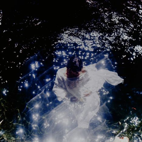 Ein Mensch in einem hellen Gewand, umgeben von schimmerndem Licht im Wasser, erzeugt eine traumhafte, geheimnisvolle Atmosphäre.