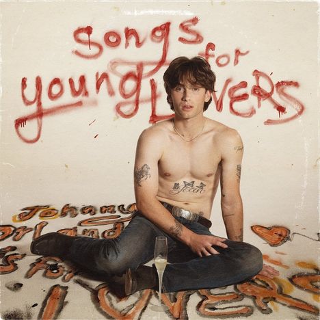 „Songs for young lovers“ steht an der Wand. Ein junger Mann sitzt oben ohne auf dem Boden, umgeben von Tattoos.