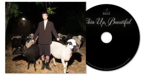 "Chin Up, Beautiful" steht auf einer CD. Ein Mensch in schwarzem Anzug hält zwei Schafe, umgeben von weiteren Schafen.