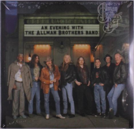 Text: "AN EVENING WITH THE ALLMAN BROTHERS BAND". Eine Gruppe von acht lächelnden Männern in Freizeitkleidung vor einem Theater.