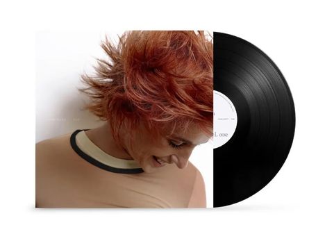 Text: "NAOMI SCOTT F.I.G" Eine Person mit kurzem, rotbraunem, wildem Haar lächelt und blickt nach unten. Sie trägt ein beige Shirt.