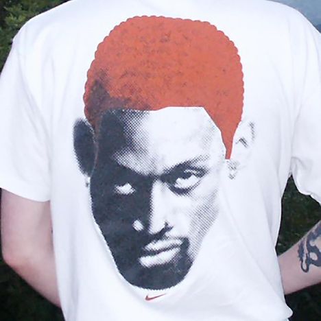 Ein weißes T-Shirt zeigt ein pixelartiges Porträt mit orangefarbenen Haaren und einem kleinen Nike-Logo darunter.