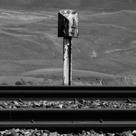 Eine alte Kilometeranzeige mit der Zahl "266" steht neben Bahngleisen in einer hügeligen, ländlichen Landschaft.