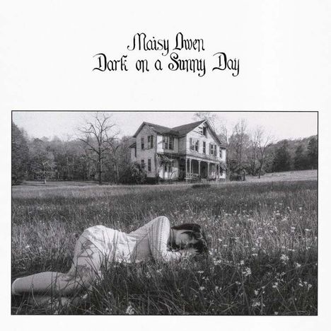 „Maisy Gwen, Dark on a Sunny Day.“ Eine Frau liegt schlafend im Gras vor einem großen alten Haus. Schwarzweiß.