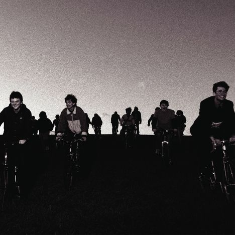 Gruppensilhouette von Menschen, die abends auf Fahrrädern fahren; dunkler Himmel im Hintergrund.