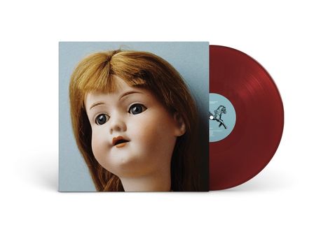 Ein rotes Vinyl und ein Albumcover mit einem großen Puppenkopf vor blauem Hintergrund.