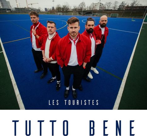TEXTE: "LES TOURISTES", "TUTTO BENE". Fünf Personen in roten Jacken auf blauem Spielfeld, schauen ernst in die Kamera.