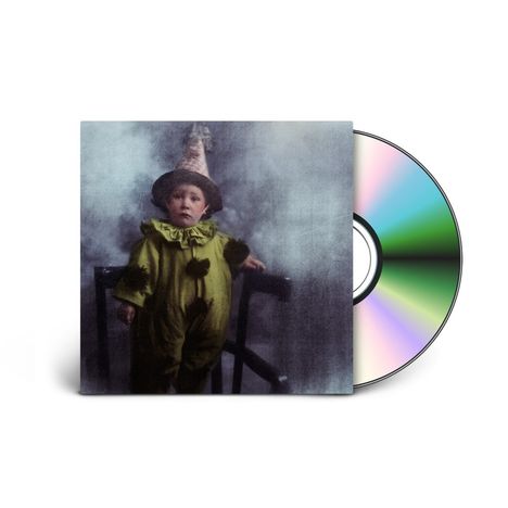 Ein kleines Kind in einem Clownskostüm steht neben einem Stuhl. Rechts daneben eine schillernde CD.
