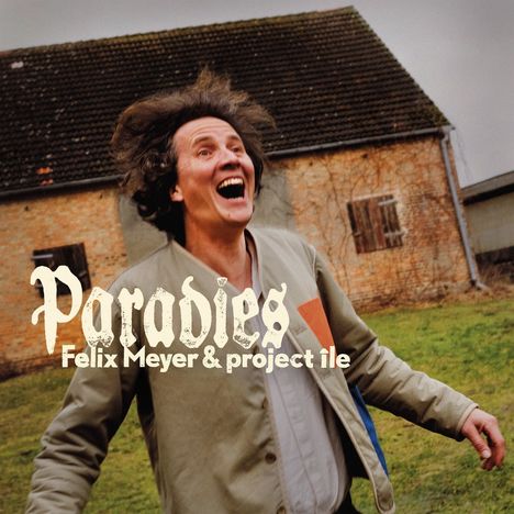 "Paradies, Felix Meyer & project ile" steht oben. Ein Mann lacht fröhlich vor einem alten Backsteinhaus.