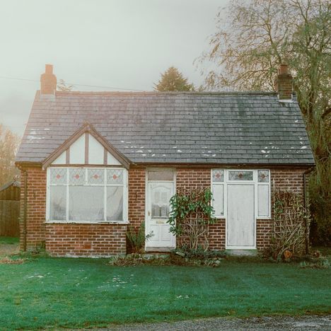 Ein kleines Backsteinhaus mit Spitzdach, weißen Fenstern und einer Tür. Vor dem Haus ist eine gepflegte grüne Rasenfläche.