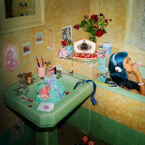 "Power to the People" steht auf einem rosa Objekt. Eine Person mit blauen Haaren und Kopfhörern in einer bunten Badewanne.