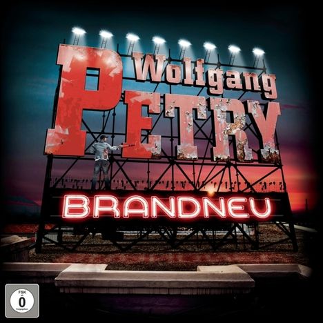 Text: "Wolfgang Petry", "BRANDNEU". Großes, beleuchtetes Schild bei Sonnenuntergang. FSK 0 unten links.