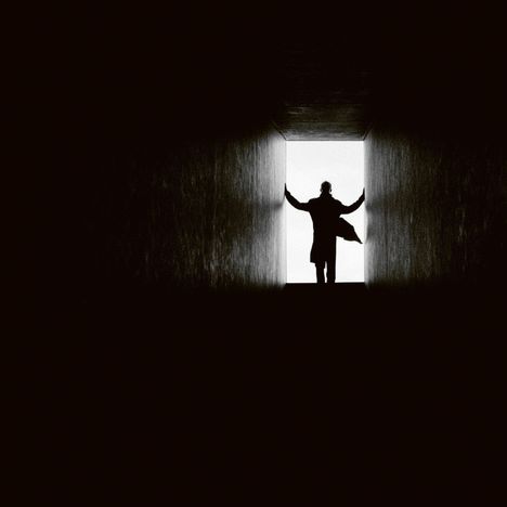 Ein Mensch steht am Ende eines dunklen Tunnels, Silhouette mit ausgestreckten Armen vor hellem Licht.