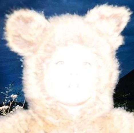 Kein Text vorhanden. Ein unscharf beleuchtetes Gesicht in einem fellähnlichen Kostüm mit Ohren, vor dunklem Hintergrund.