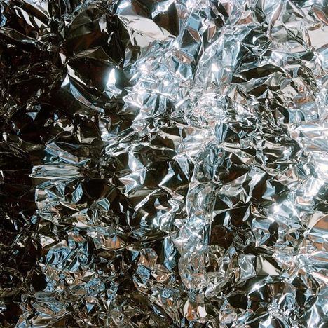 Zerknitterte Aluminiumfolie reflektiert das Licht, wodurch ein glänzender, chaotischer Effekt entsteht.
