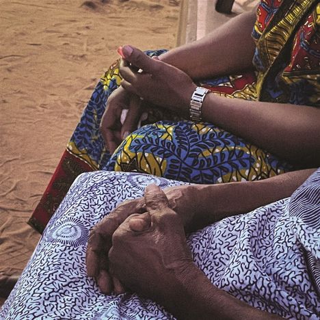 Eine Person trägt farbige Kleidung mit lebhaften Mustern; Hände ruhen entspannt im Schoß.