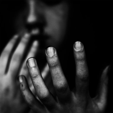Keine Texte sichtbar. Im Vordergrund sind unscharfe, leicht schmutzige Hände zu sehen. Eine Person im Hintergrund.